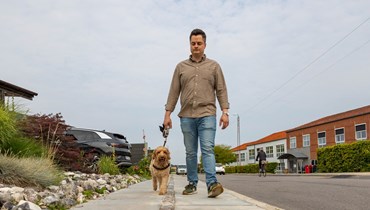 Mand der går udenfor med sin hund i snor. Man ser dem forfra gå mod kameraet.