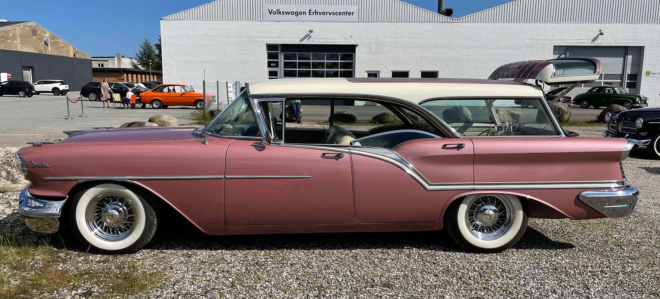 En rosa klassisk bil holder parkeret. Man ser den fra siden. 