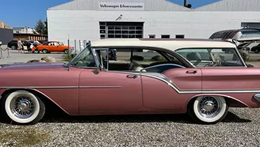 En rosa klassisk bil holder parkeret. Man ser den fra siden.