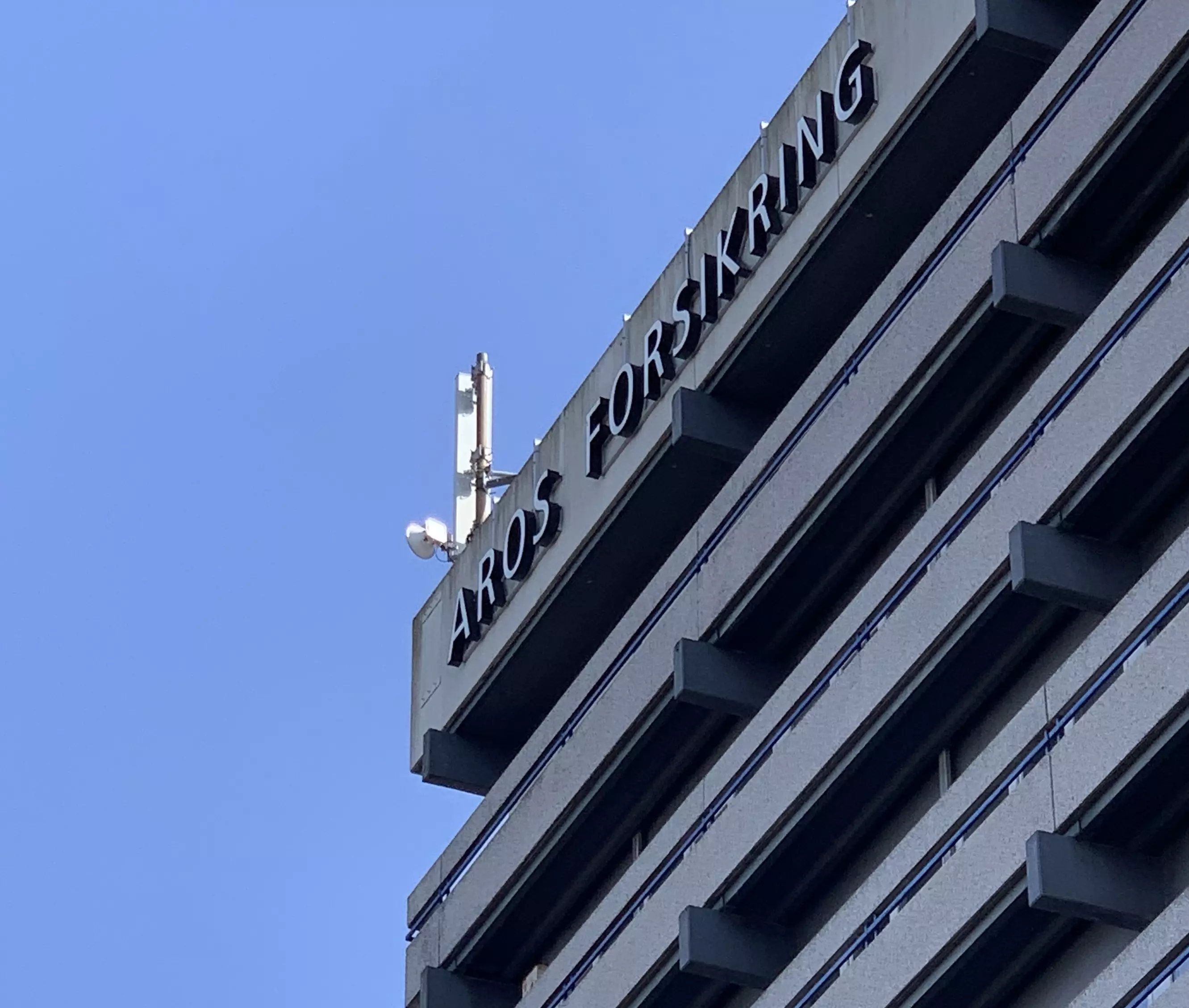 På billedet ses toppen af en bygning, hvor Aros Forsikrings logo er skrevet.