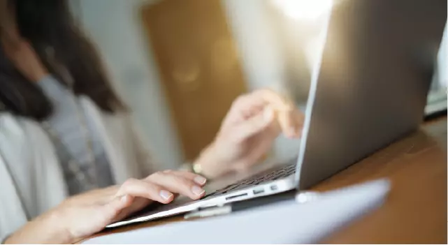 Closeup af en kvindes hænder på tastatur.