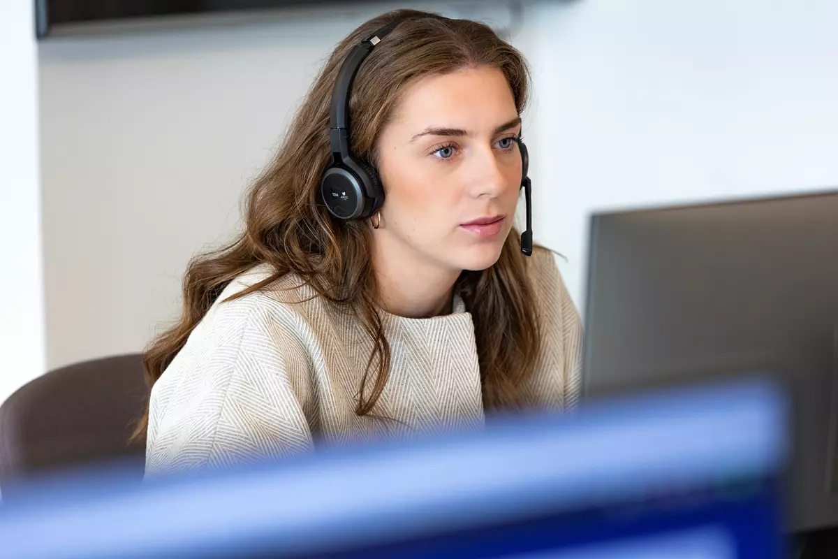 En kvinde iført headset sidder på et kontor og kigger fokuseret på en computerskærm