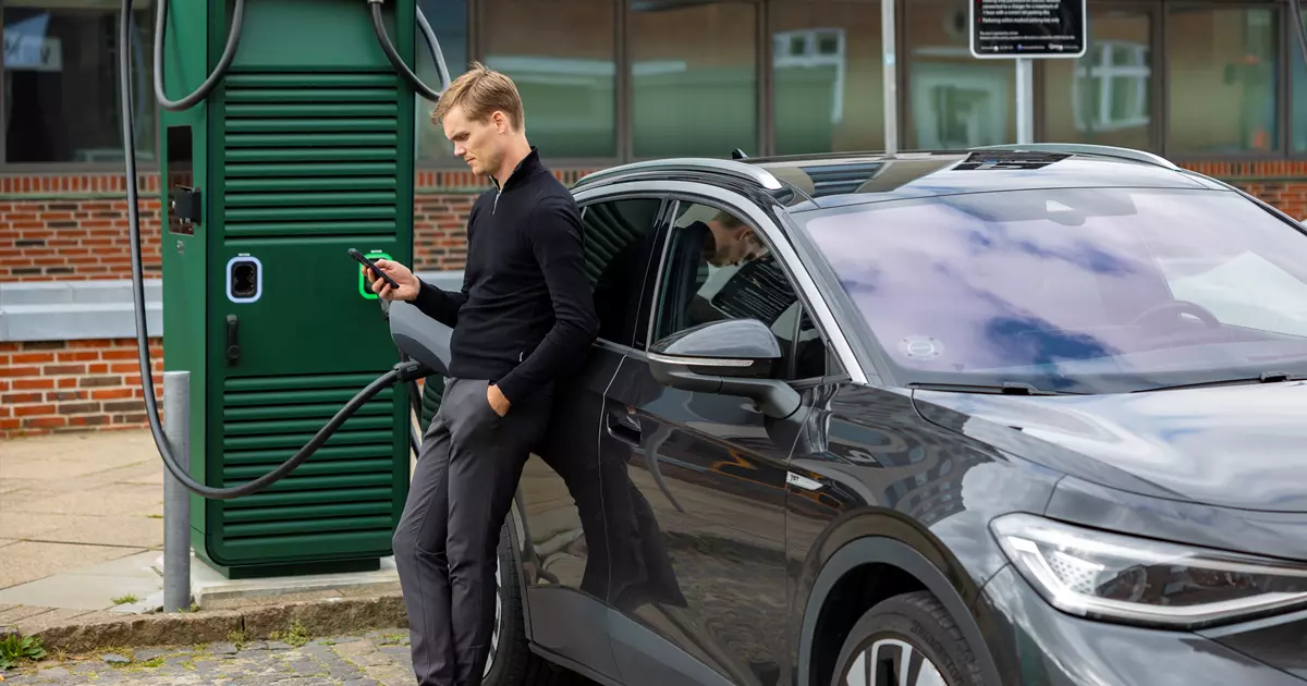Mand oplader sin elbil der holder parkeret udenfor.