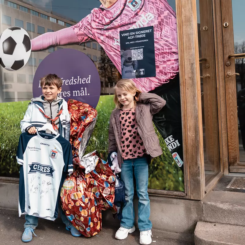 Børn med AGF trøje og kæmpe påskeæg foran Aros Forsikring butiksvindue
