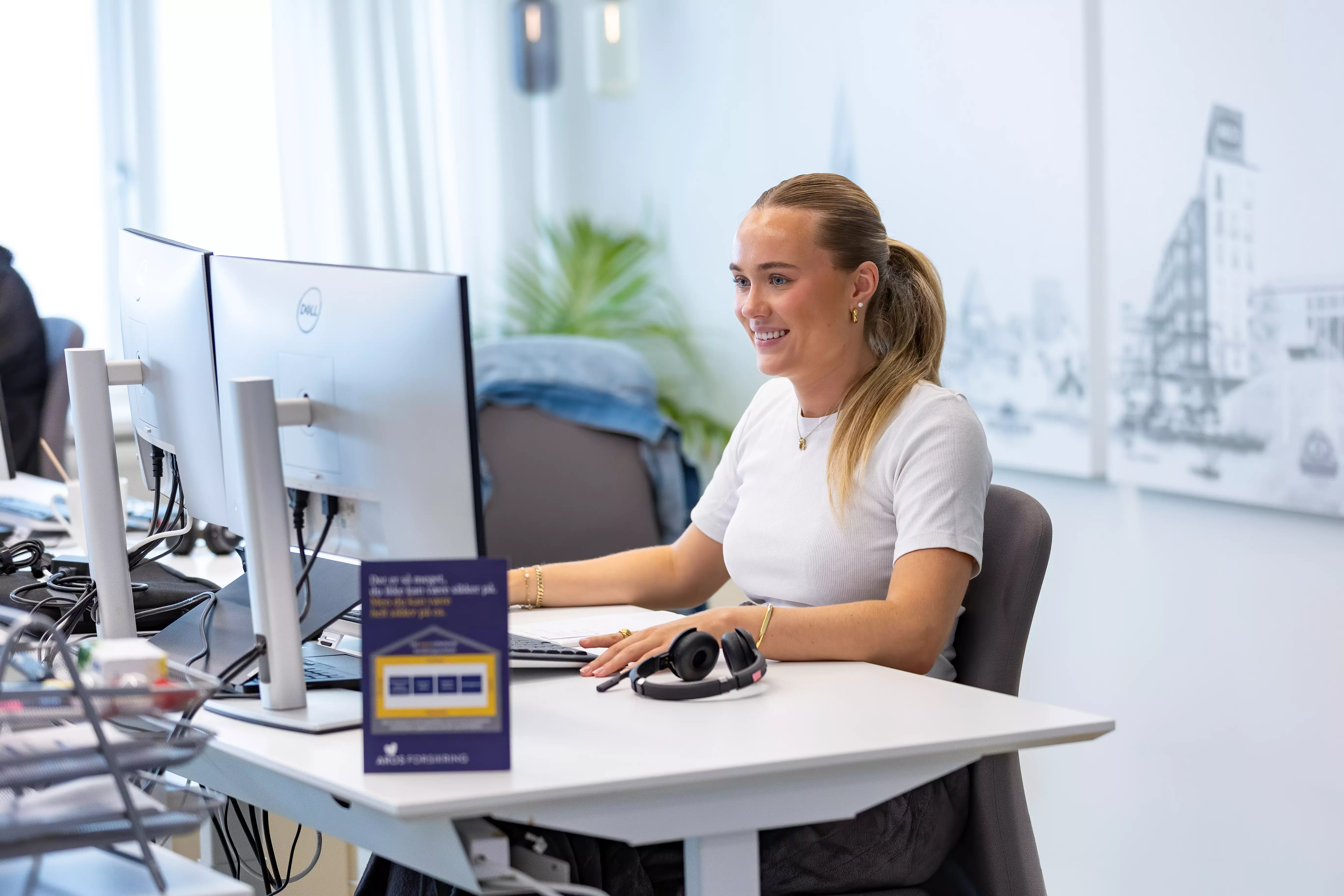 En kvinde hos Aros Forsikring sidder foran sin computer og smiler
