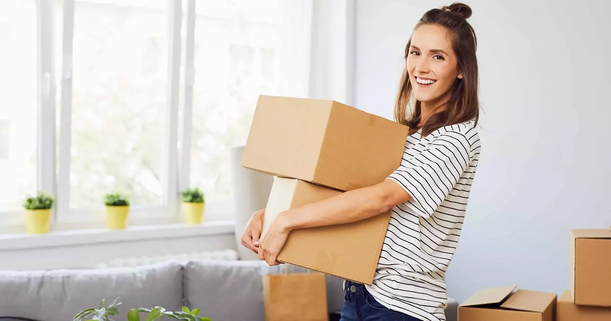 En kvinde løfter flyttekasser. I baggrunden ses en stue og flere flyttekasser.