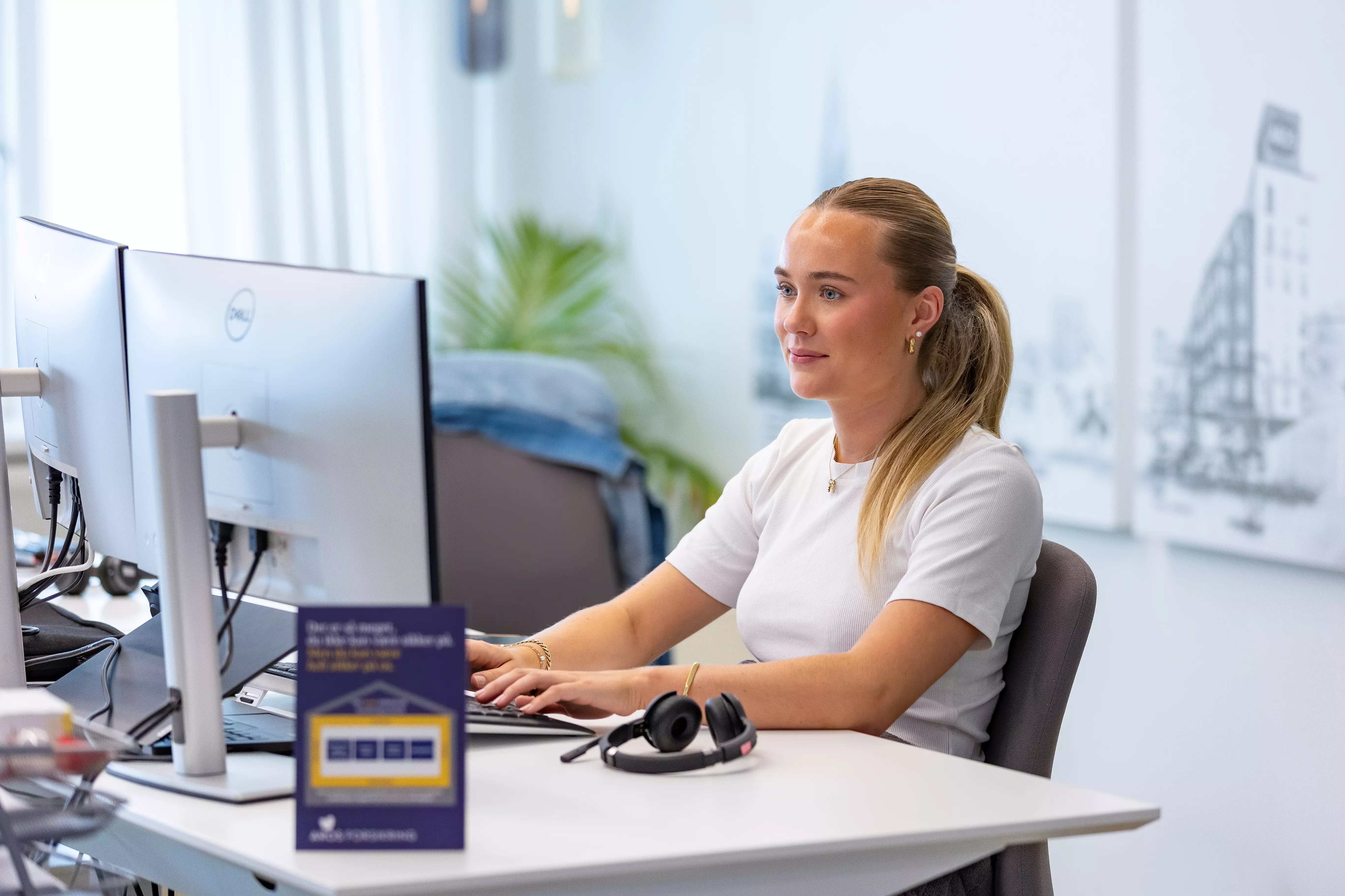 En ung kvnde sidder på kontor foran en computer og arbejder med et smil på læben