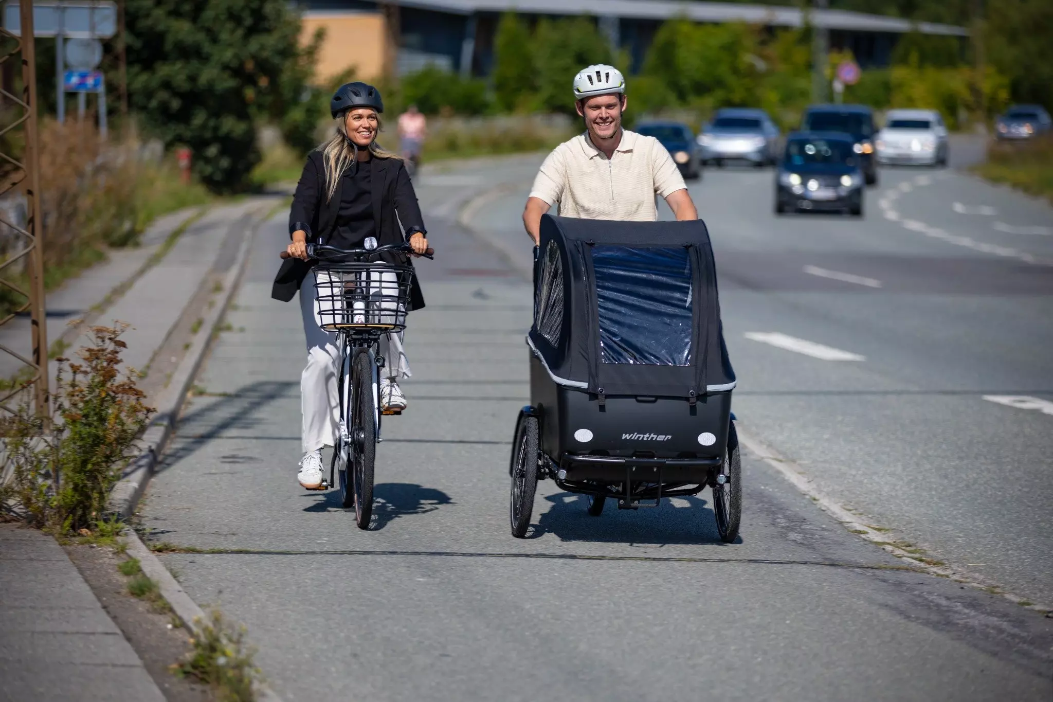 En mand og en kvinde kommer cyklende på en vej. De smiler.