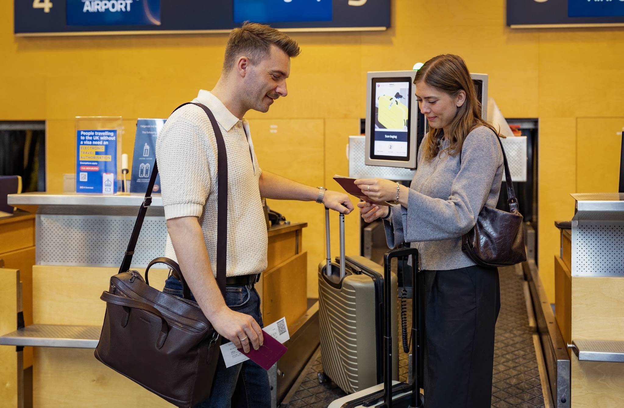 To rejsende står ved bagageindlevering i lufthavnen med kufferter, pas og boardingkort.