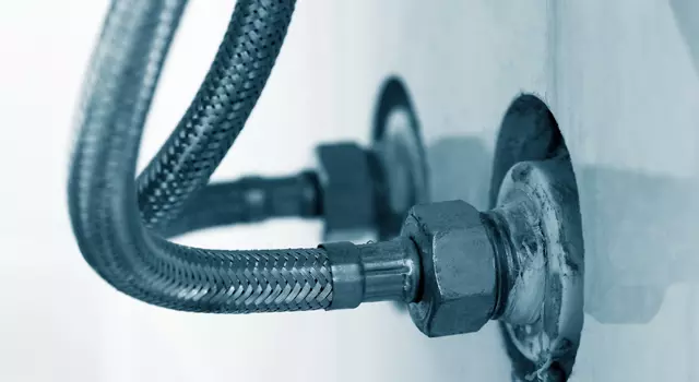 Nærbillede af to fleksible metalrør tilsluttet vægmonterede fittings, sandsynligvis en del af et VVS-system.