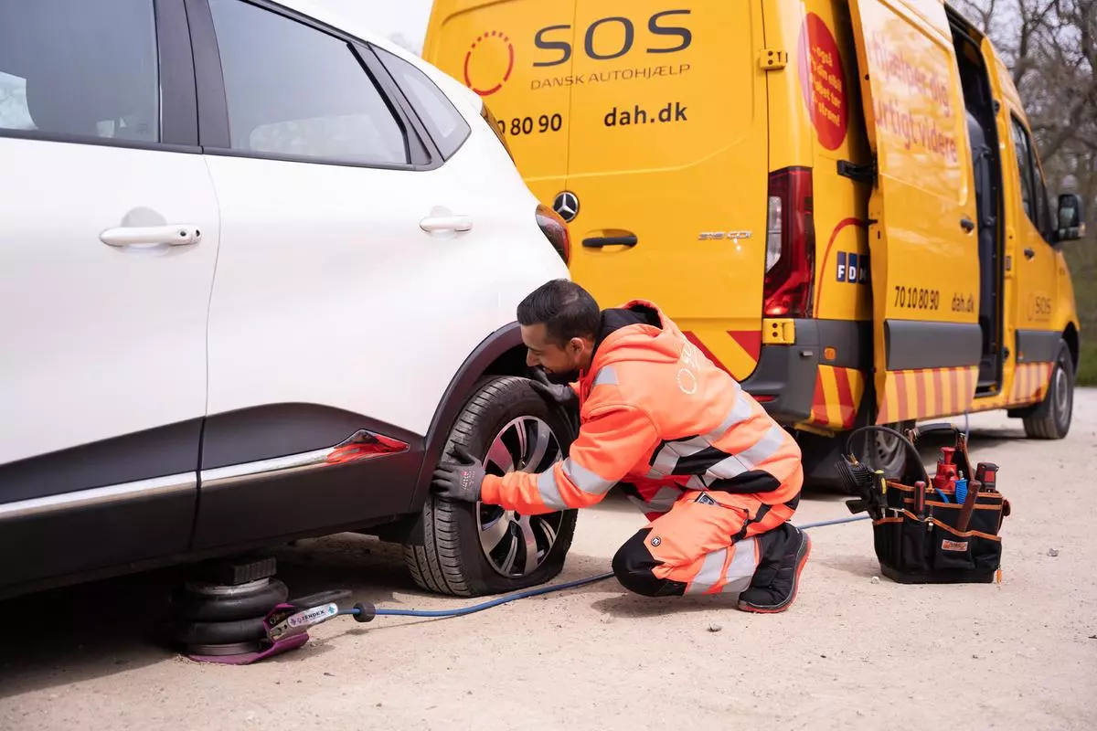 En medarbejder fra SOS Dansk Autohjælp skifter dæk på en bil der er punkteret.