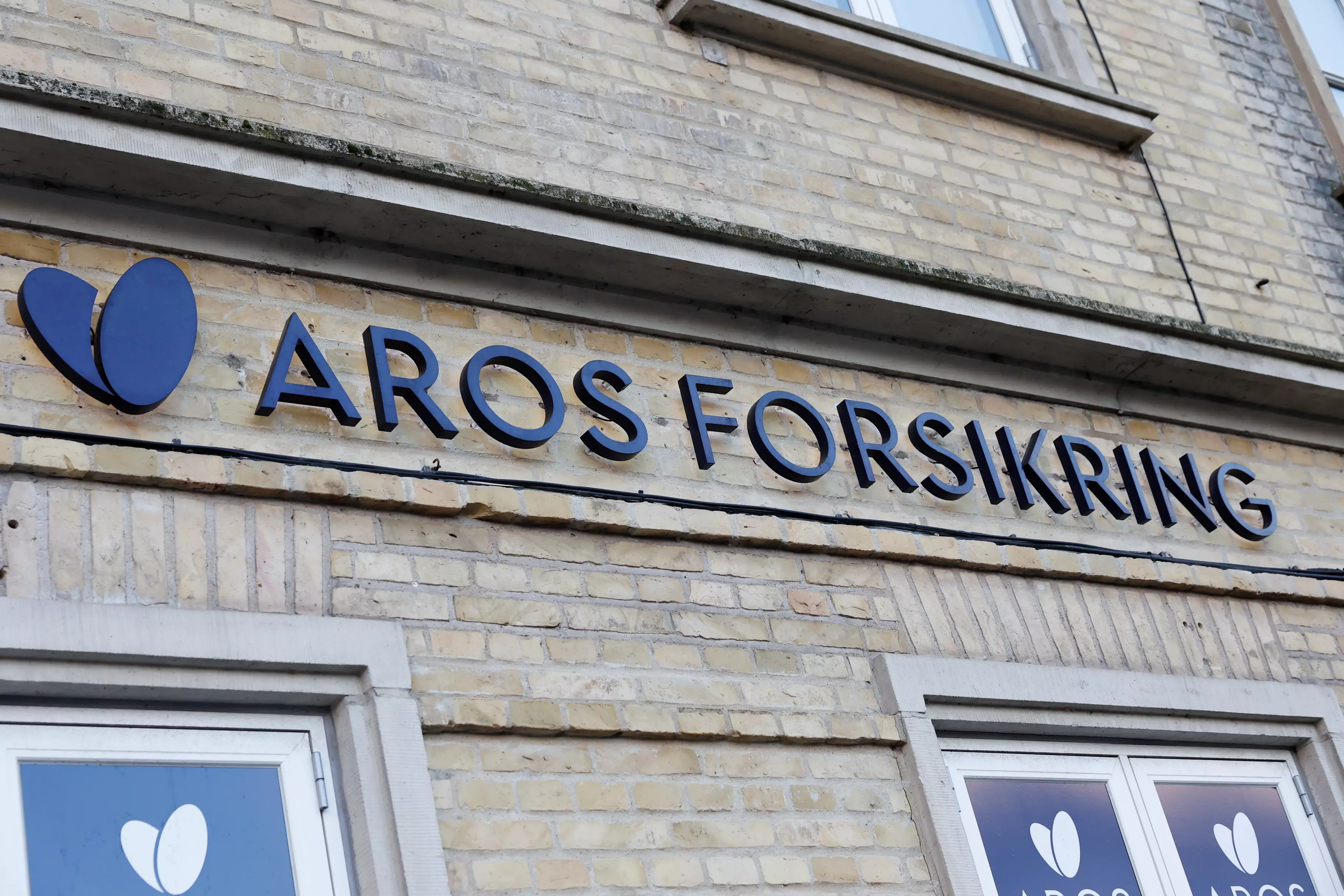 En bygning set i closeup udefra. Man ser skiltet Aros Forsikring og logo.