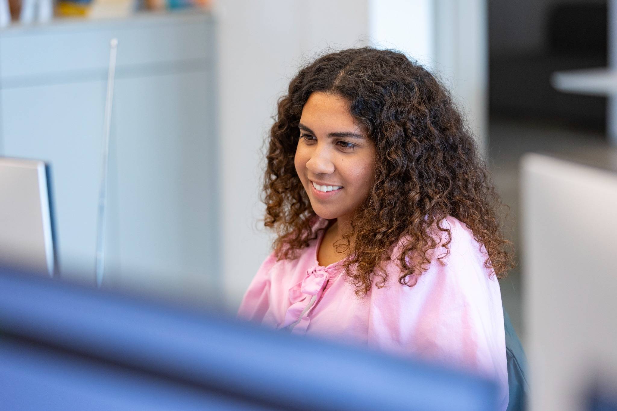Medarbejder med krøllet hår ved skrivebordet, fokuseret på computerskærmen