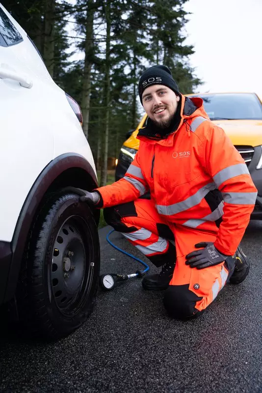 En medarbejder fra SOS Dansk Autohjælp skifter dæk på en bil der er punkteret.