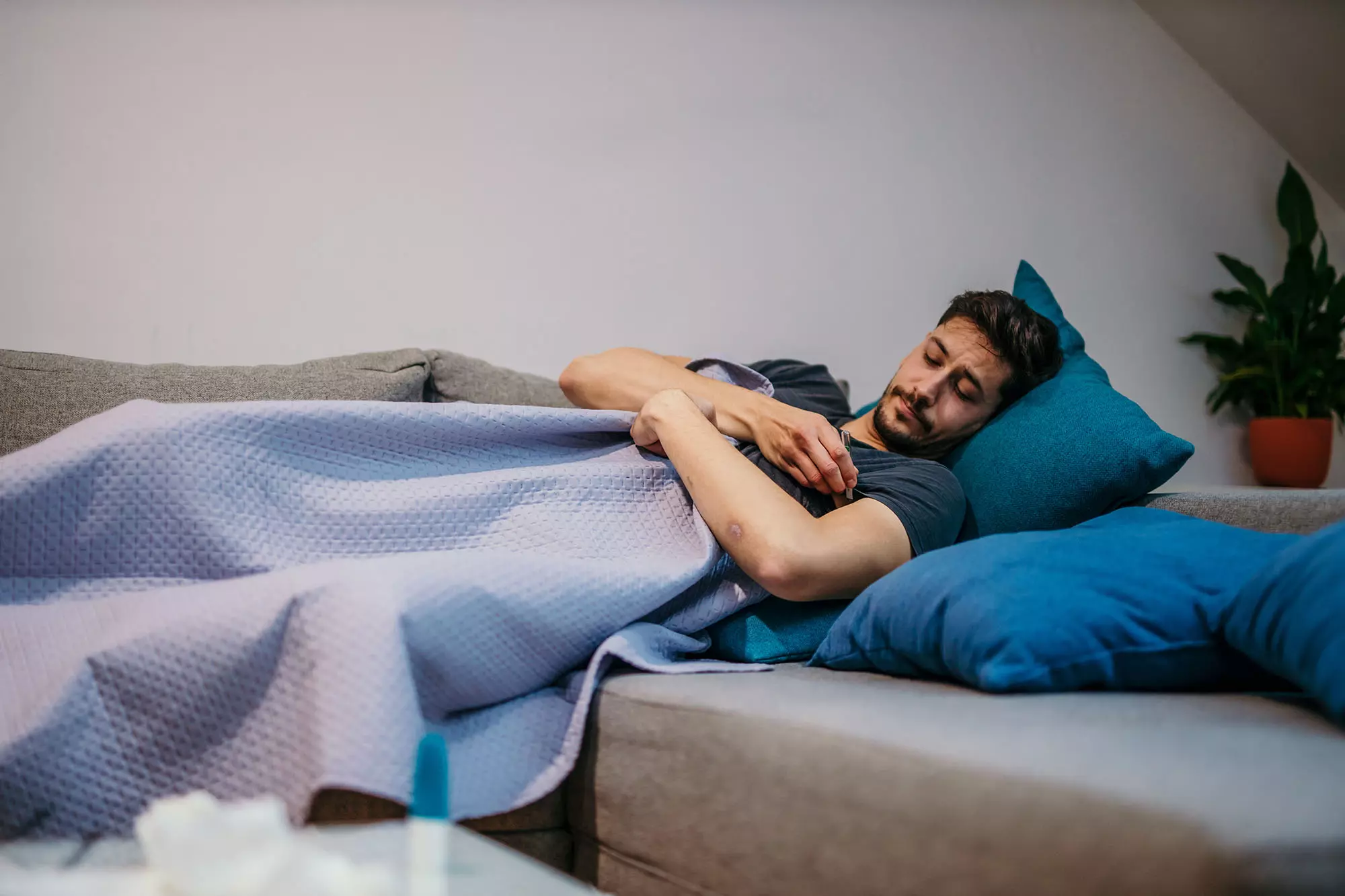 En mand lægger på sofaen under et tæppe og sover.