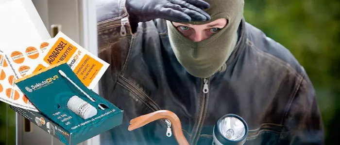 En person iført elefanthue og læderjakke kigger ind gennem et vindue og skygger for solen med hånden. Foran personen ses sikkerhedsprodukter som mærkater, en sikringslås og en lampe.