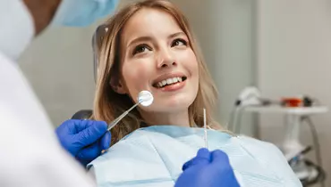 En kvinde er til tandlæge og man ser hende sidde i stolen. Hun smiler og er klar til behandling.