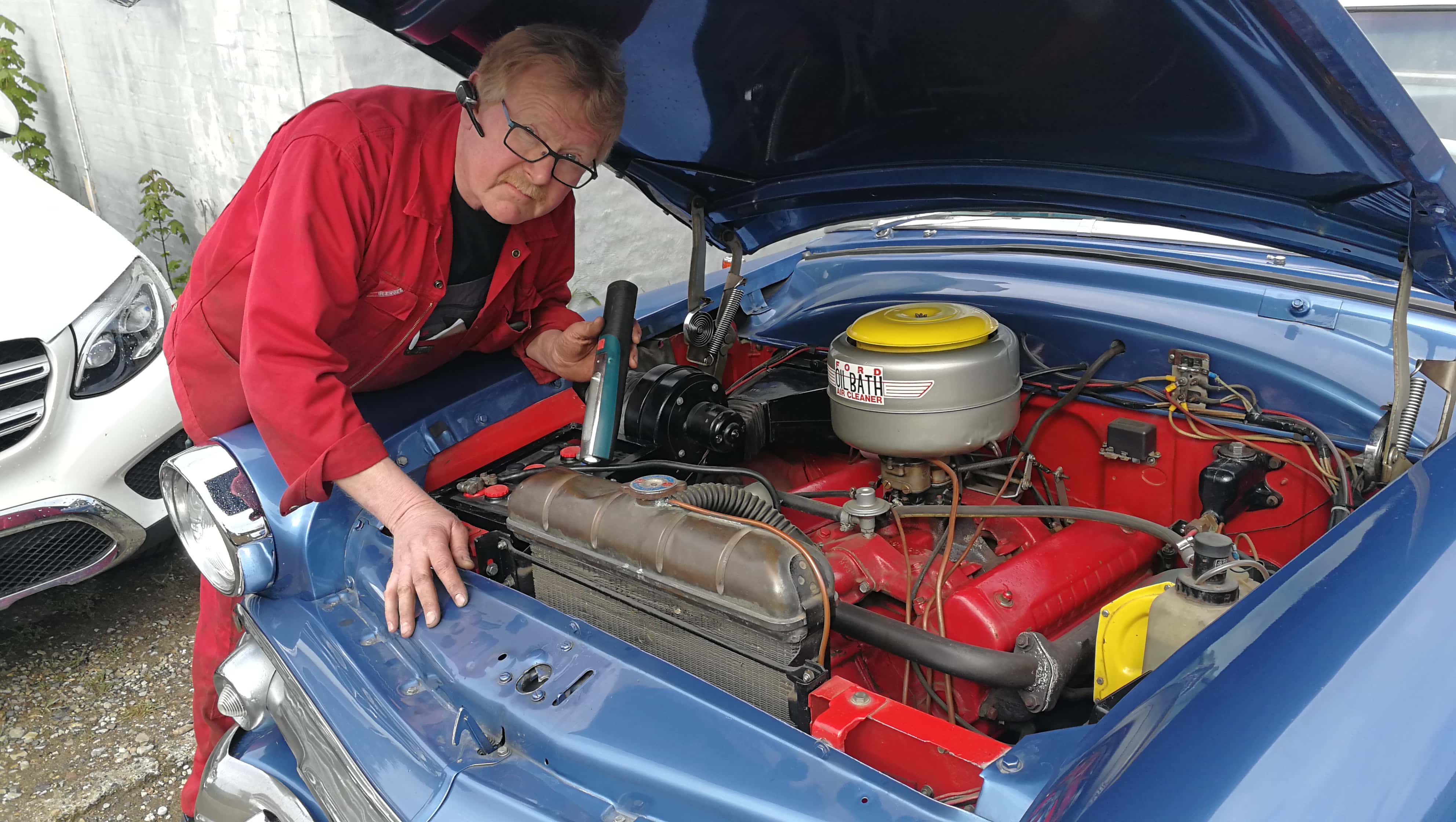 En mekaniker der ordner noget på motorhjælpen i en bil.