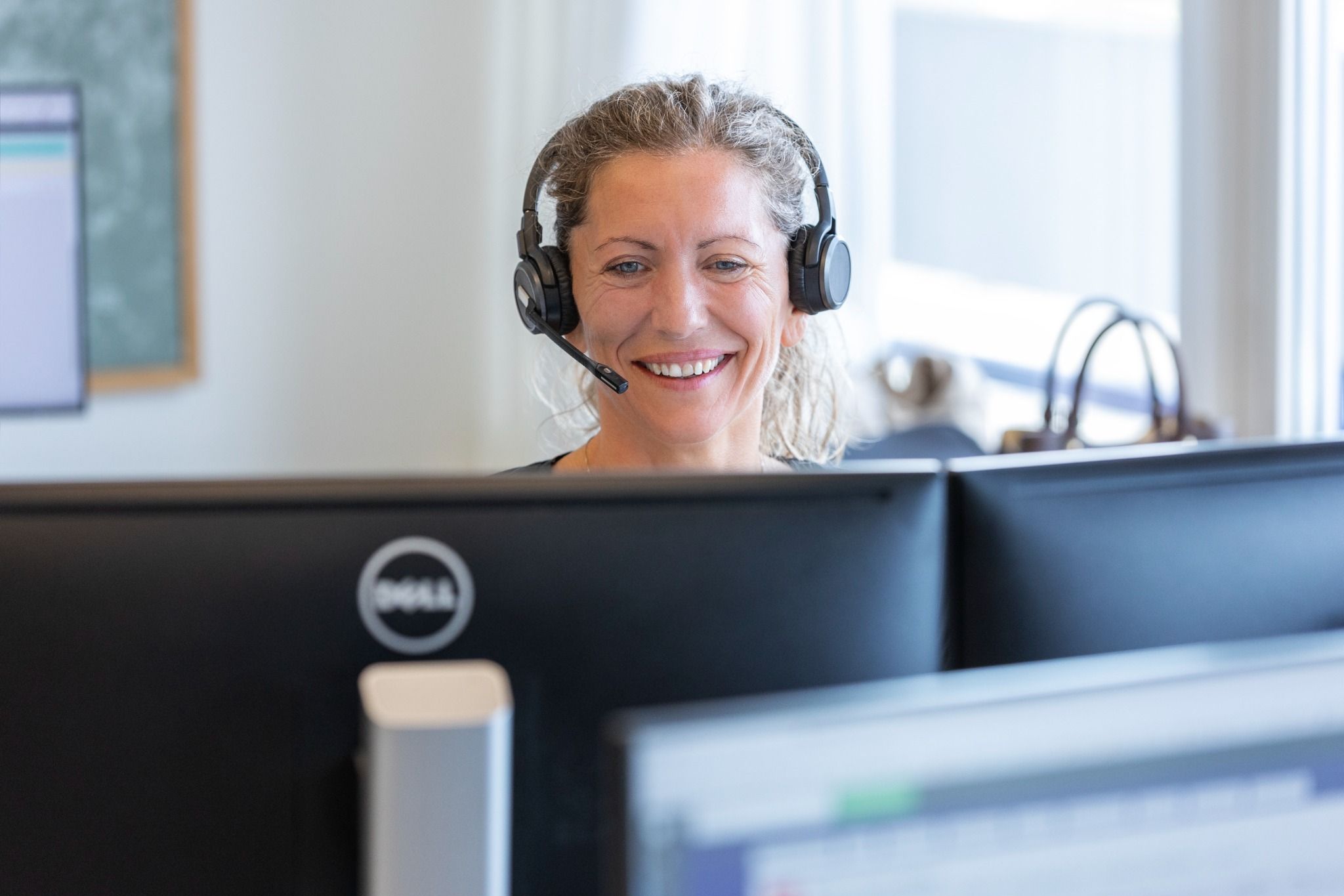 Skade-medarbejder med headset smiler foran to computerskærme