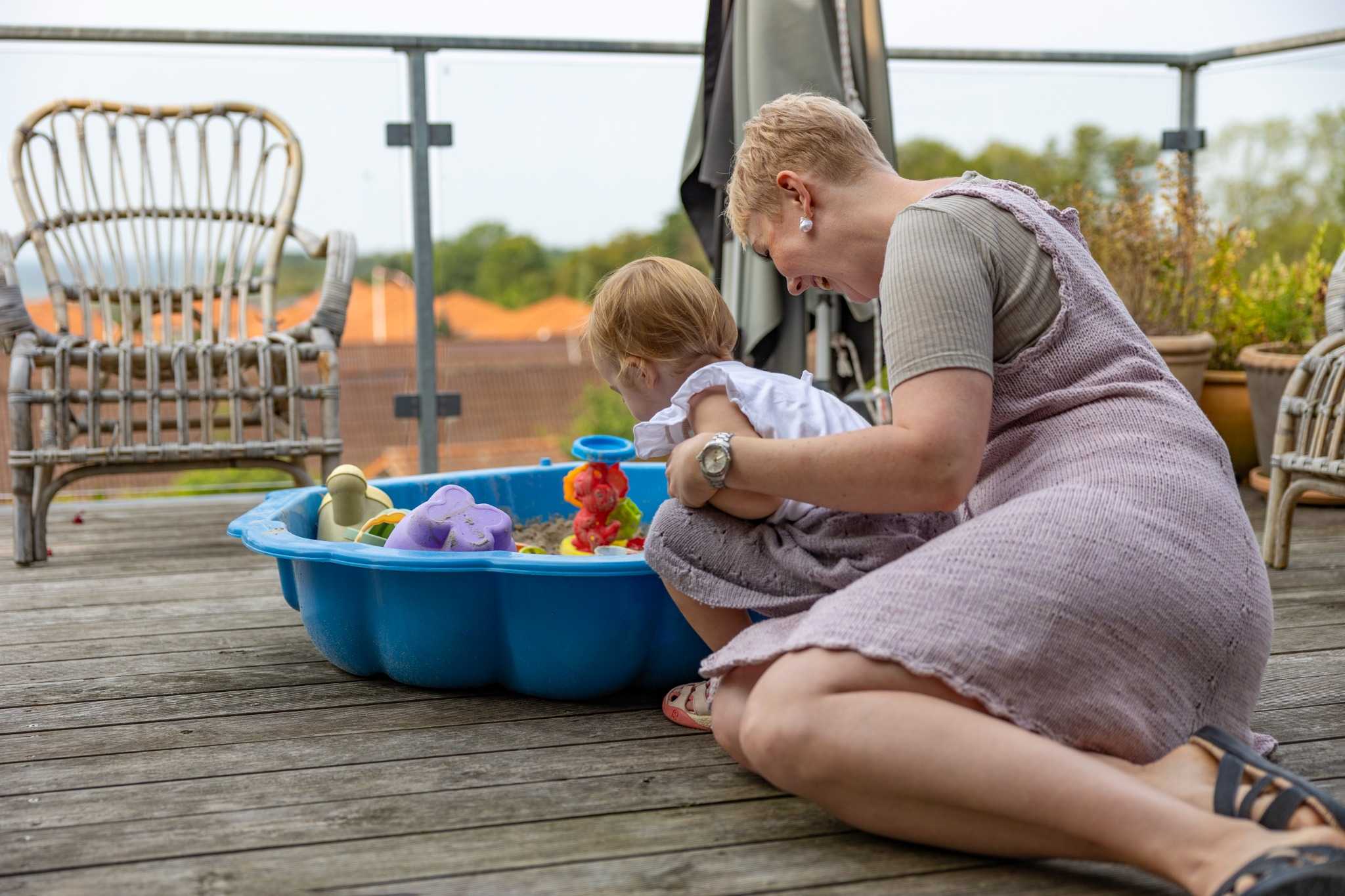 En kvinde og et barn sidder og kigger i en blå sandkasse.