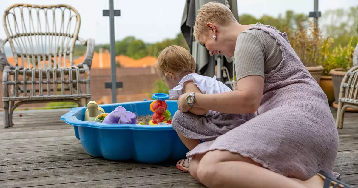 En kvinde og et barn sidder og kigger i en blå sandkasse.