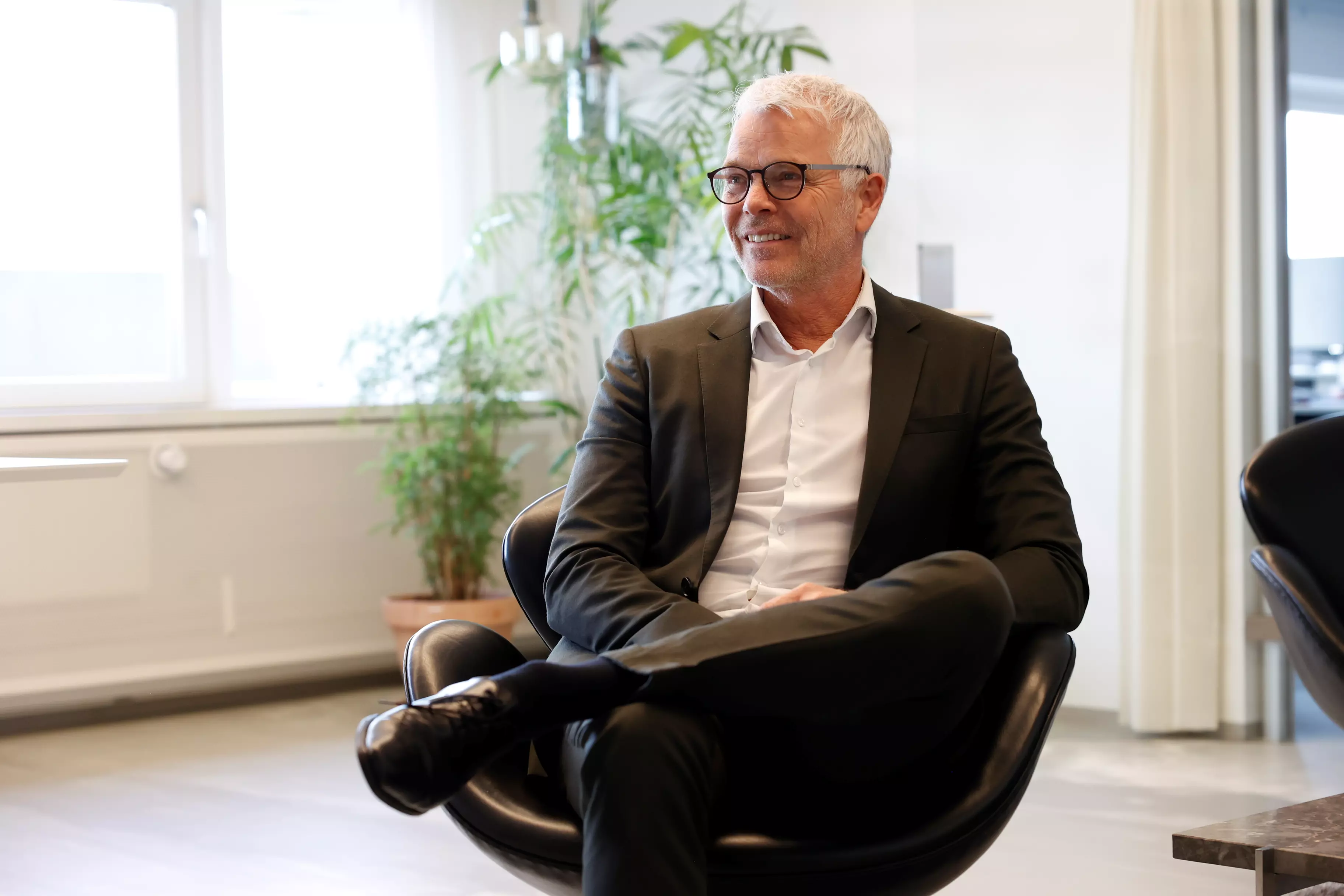 Mand i jakkesæt sidder i designerstil på et kontor. Han har et venligt udtryk og smiler let.