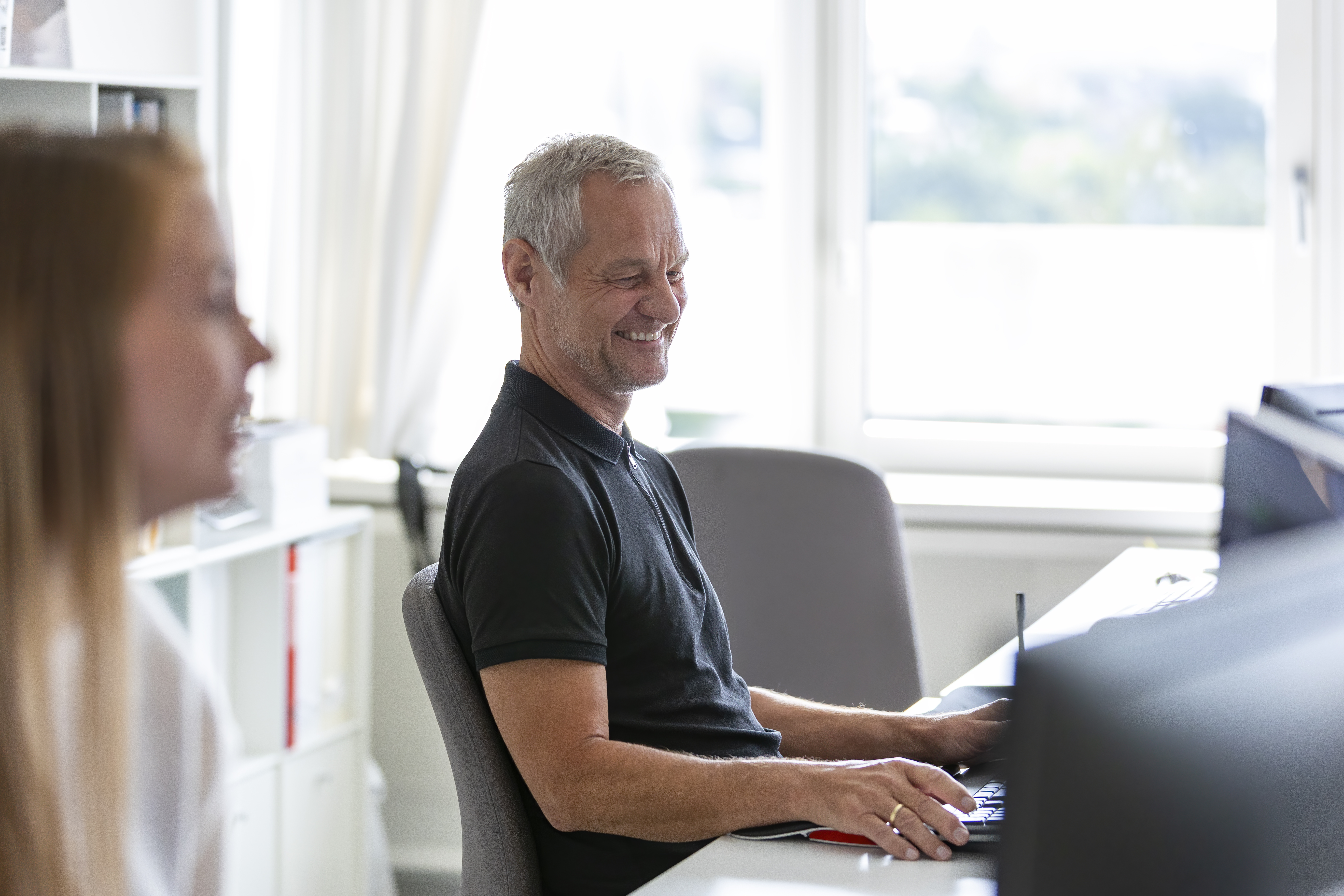 En mand sidder og smiler ved sit skrivebord