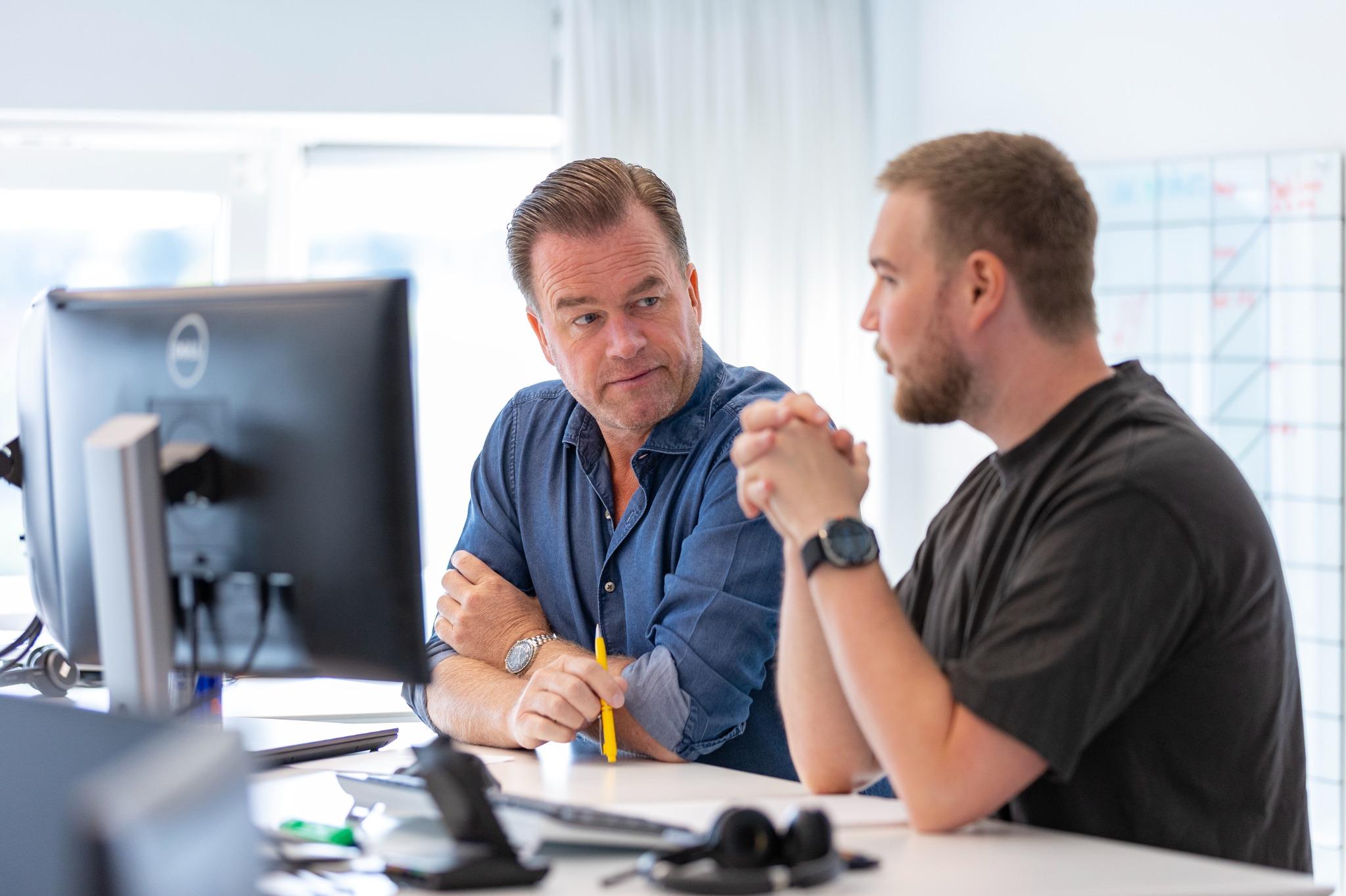 To kolleger i dialog ved skrivebord, mens de kigger på computerskærm