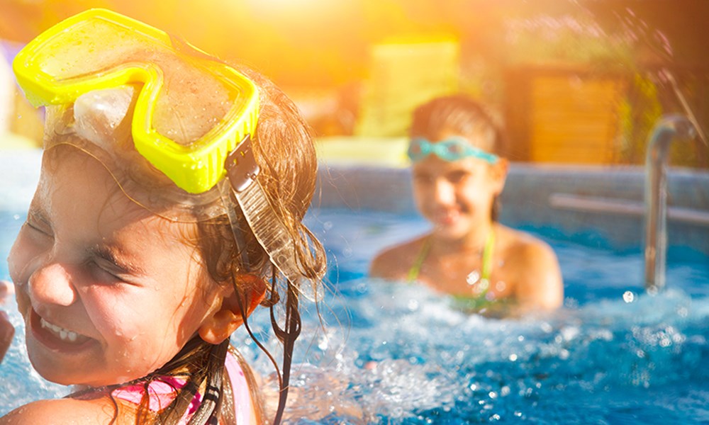 To børn der plasker i en pool. De smiler og har det sjovt. 
