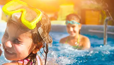 To børn der plasker i en pool. De smiler og har det sjovt.