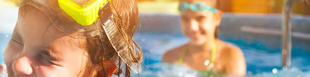 To børn der plasker i en pool. De smiler og har det sjovt.