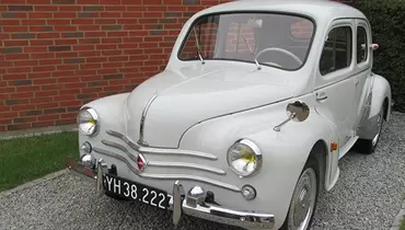 Billedet viser en hvid bil der holder i en indkørsel.