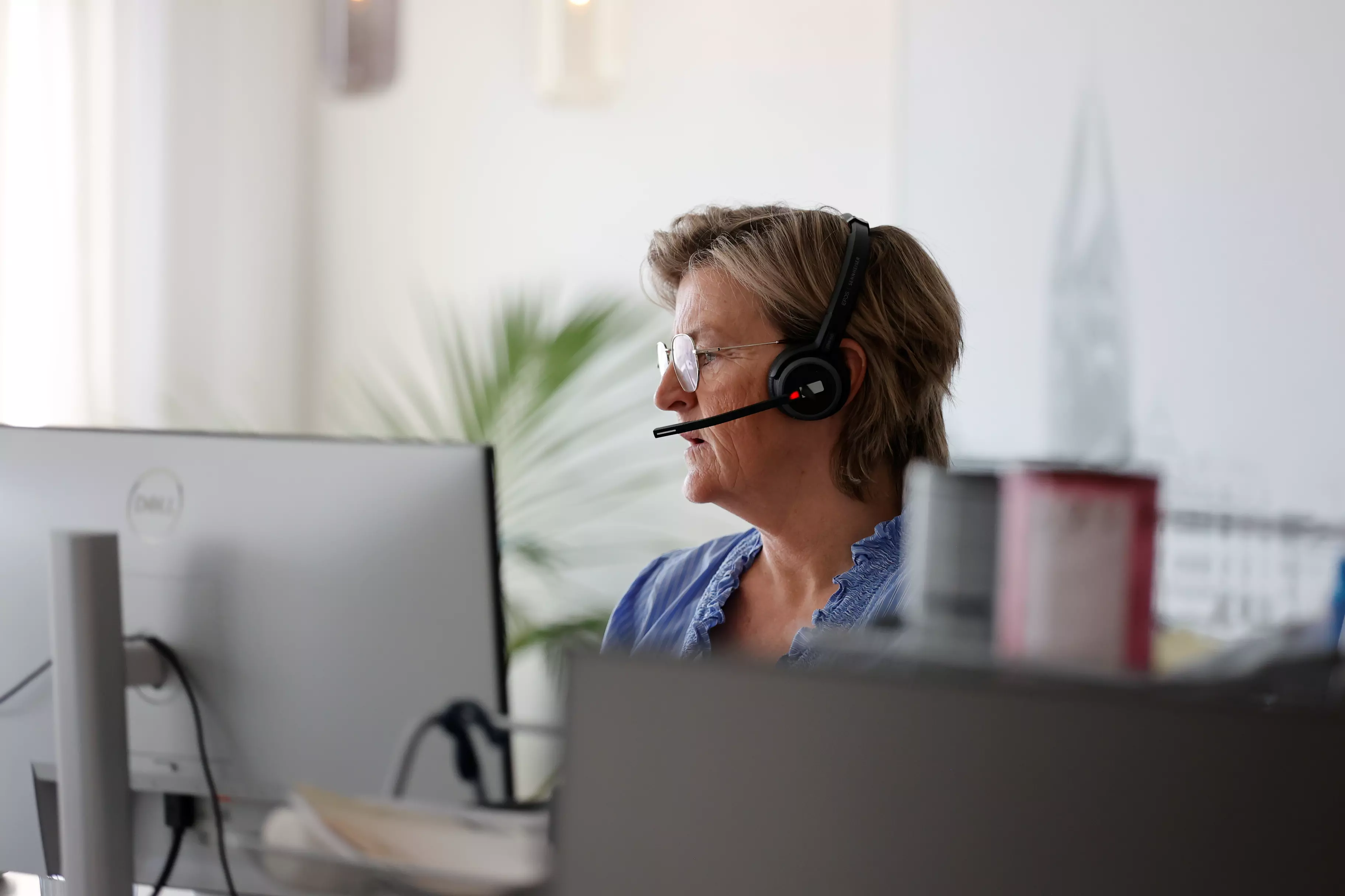 En kvinde sidder foran en computer og taler i telefonen via sit headset.