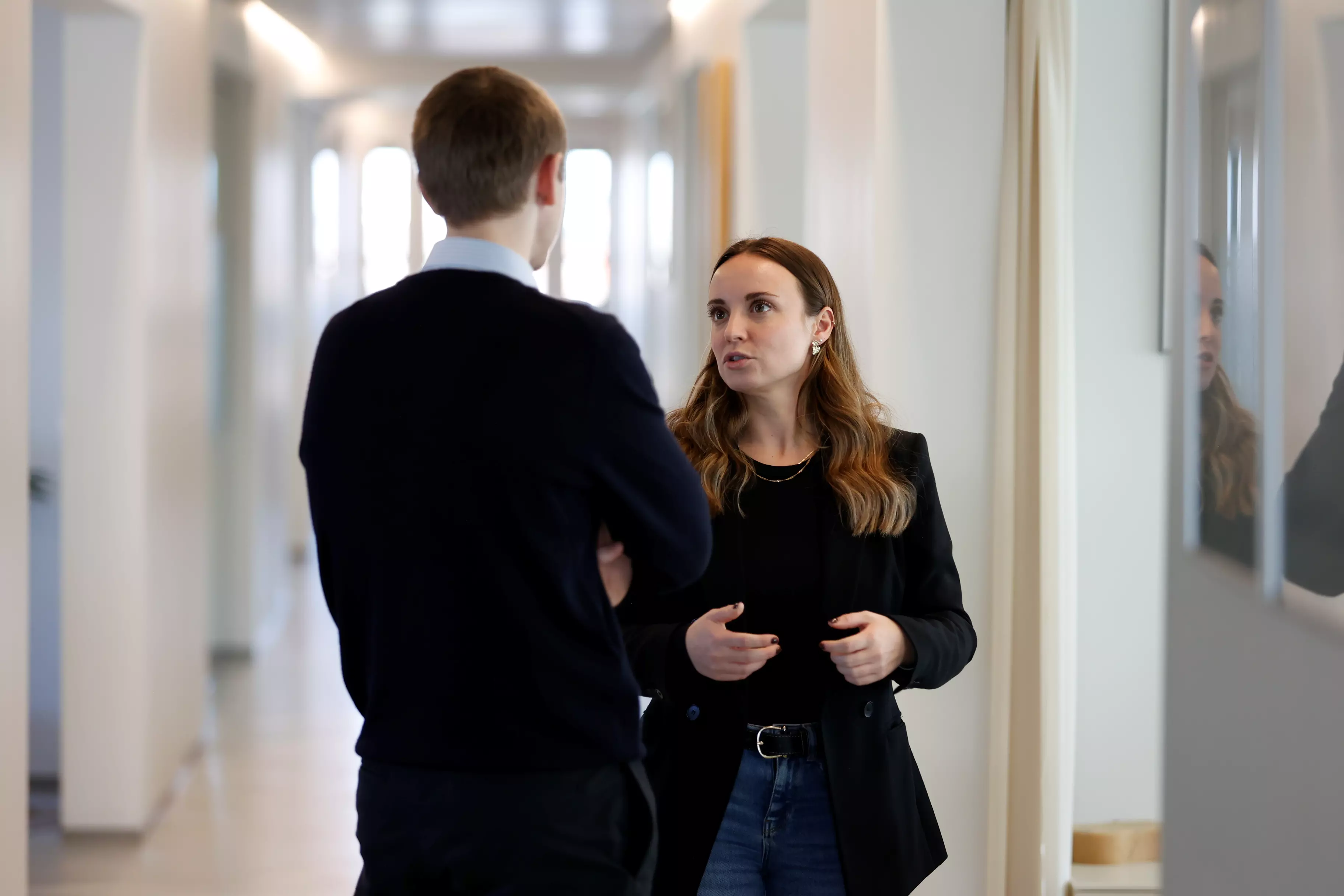 To personer står på gangen i et kontormiljø og taler sammen.