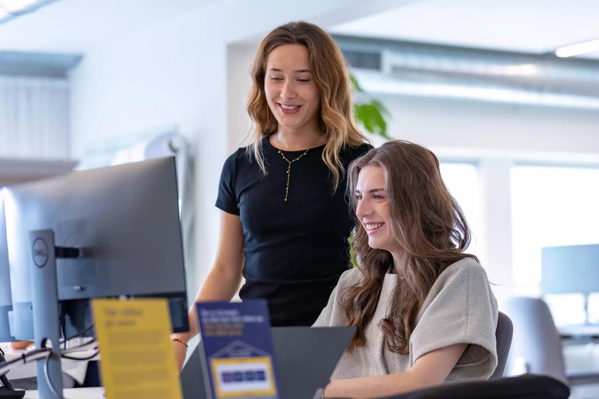 Stående kollega hjælper siddende medarbejder med headset foran skærm