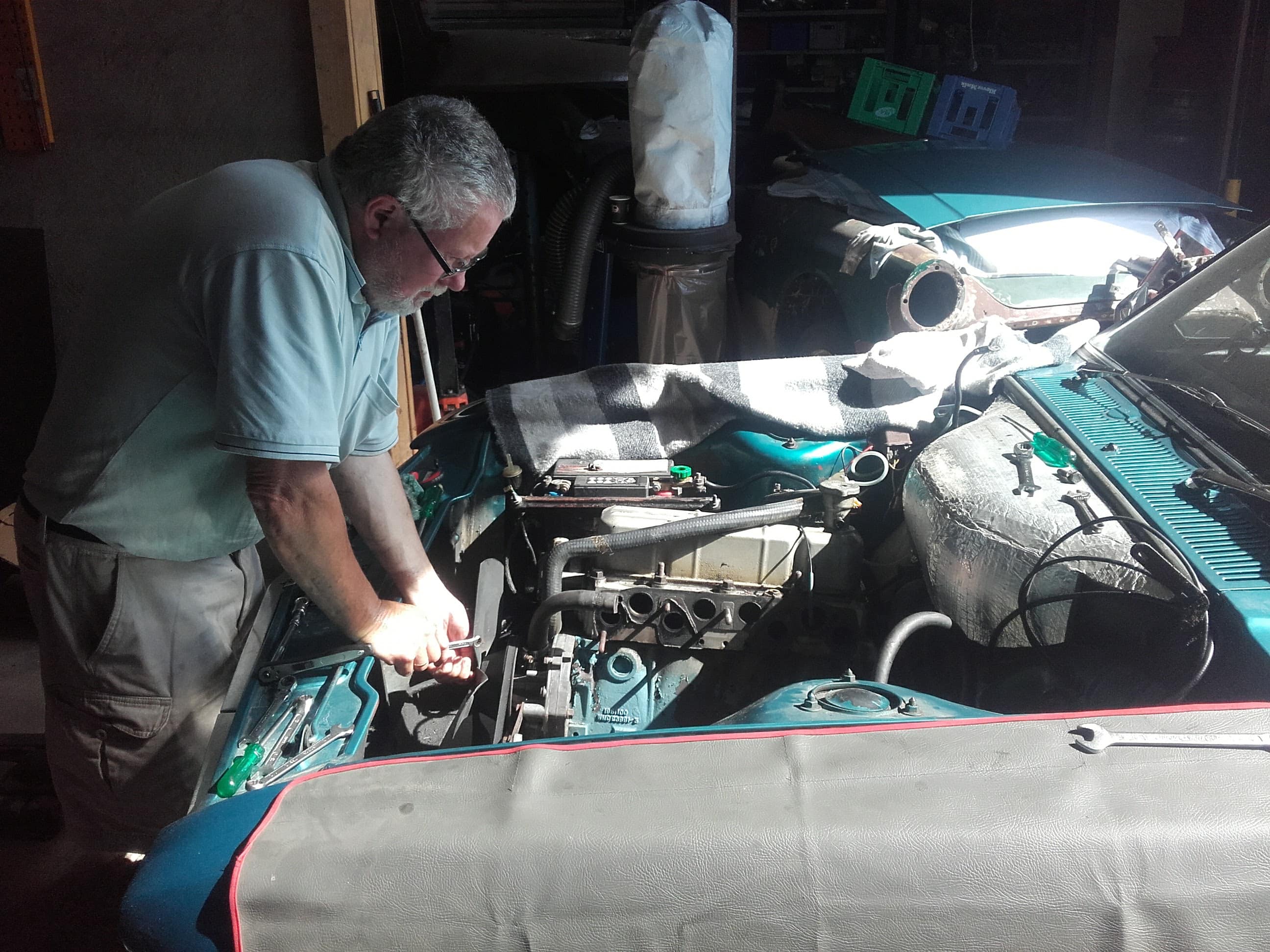 En mekaniker kigger ned i motorhjelmen på en bil og er igang med at reparere noget.