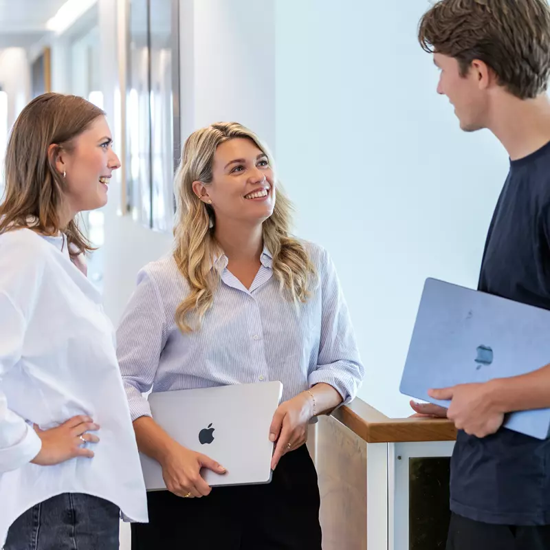 To kvinder og en mand står og snakker i et kontormiljø