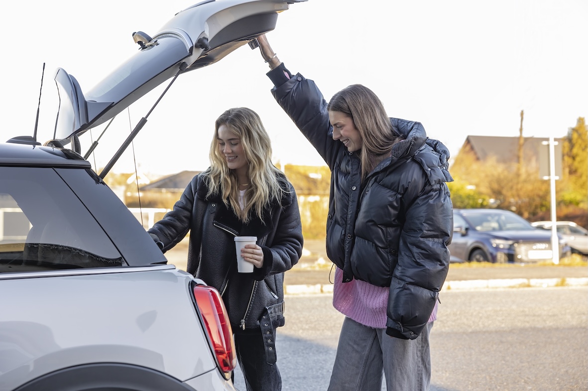 To yngre mennesker, der smiler og har åbnet bagsmækken til en bil. De smiler og der er god stemning.