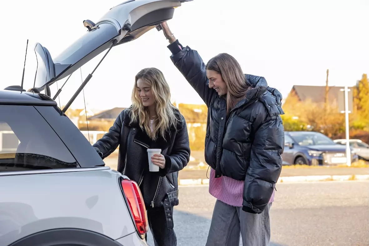 To yngre mennesker, der smiler og har åbnet bagsmækken til en bil. De smiler og der er god stemning.
