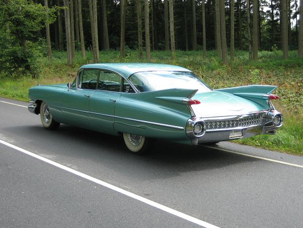 En klassisk mintgrøn Cadillac sedan fra slutningen af 1950'erne eller begyndelsen af 1960'erne, fotograferet ved en skovvej. Bilen har de karakteristiske finner bagtil, skinnende kromdetaljer og hvide dæksider, der fremhæver dens elegante og tidløse design. Med de store dimensioner og unikke linjer er den en ægte repræsentant for amerikansk bilkultur fra denne æra.