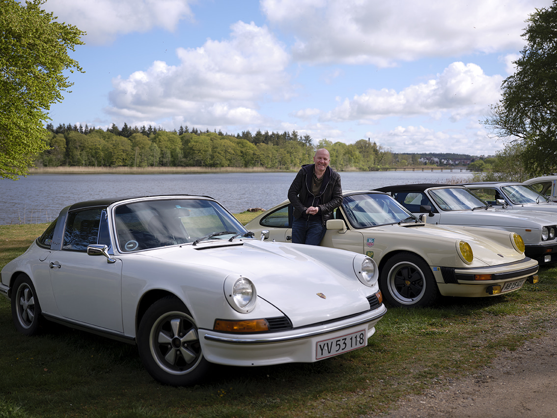 Billede af en klassisk bil og en mand der læner sig op af bilen og smiler.