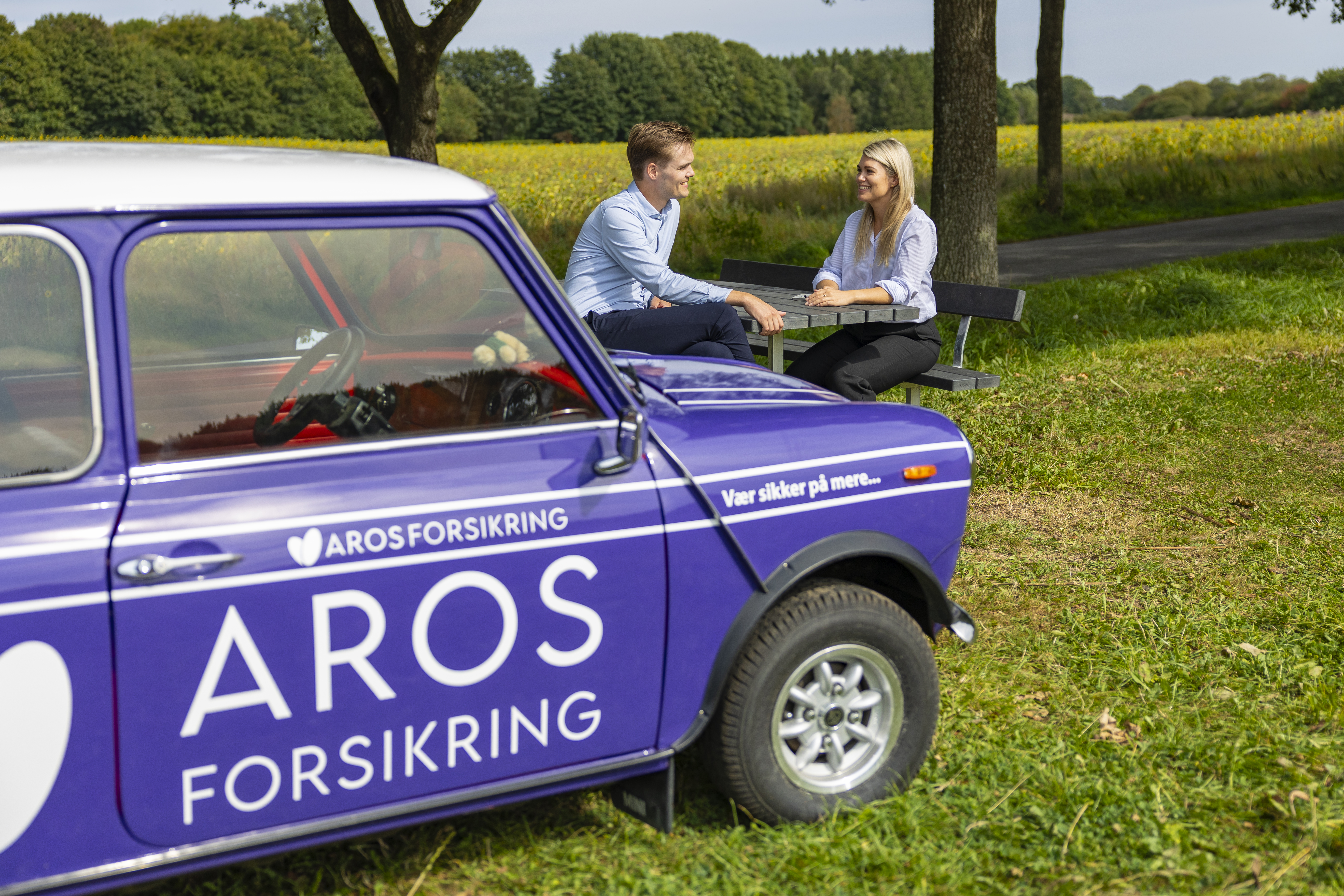 Par sidder ved deres veteranbil med Aros Forsikring logo