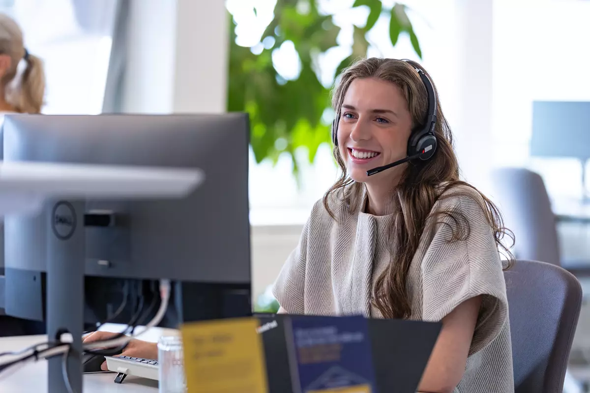 En kvinde snakker i telefon med headset og smiler