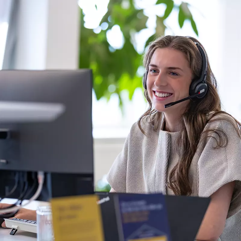 En kvinde snakker i telefon med headset og smiler