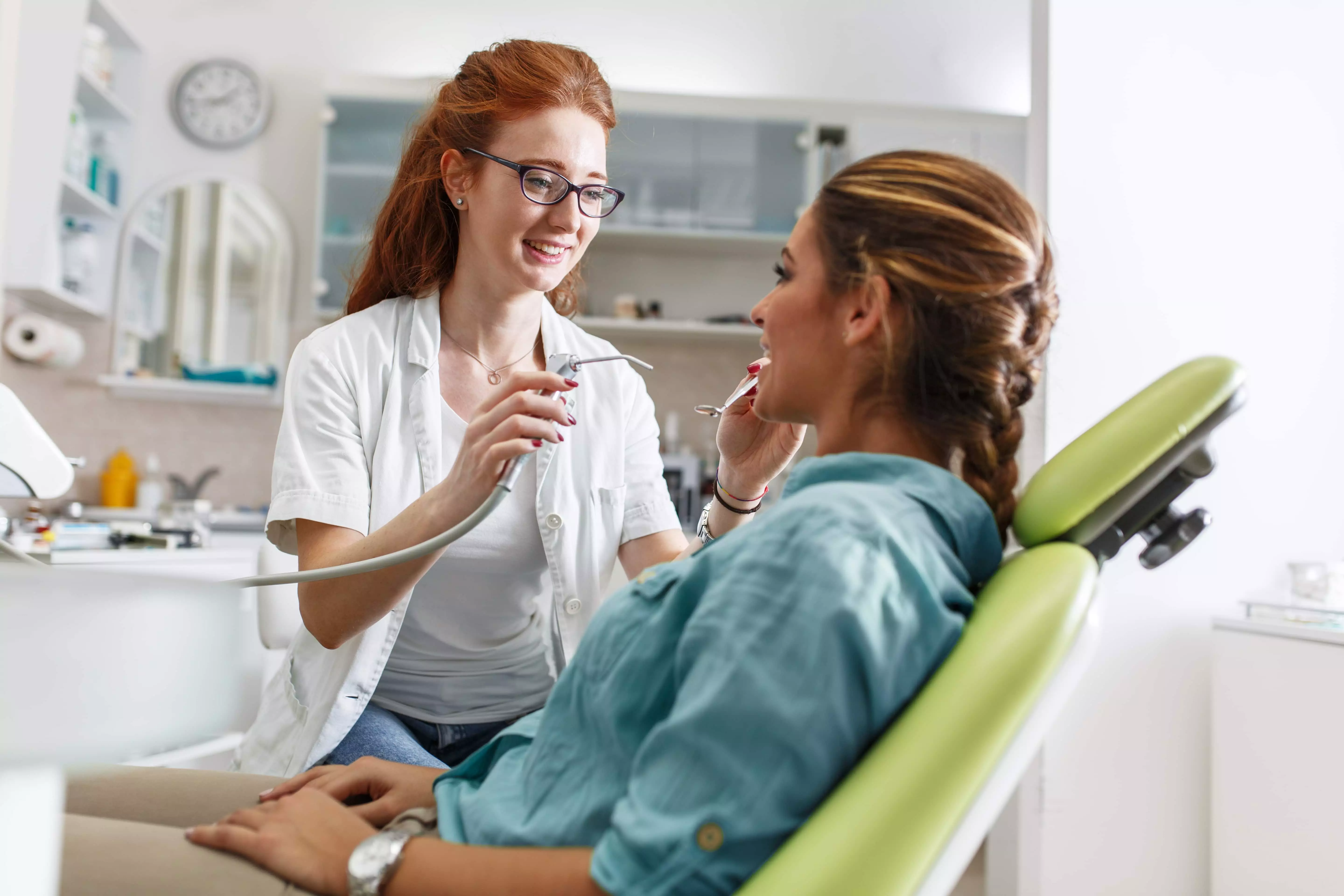 En kvinde sidder i en tandlægestol og får lavet en behandling af en tandlæge. Baggrunden er en tandlægeklinik.