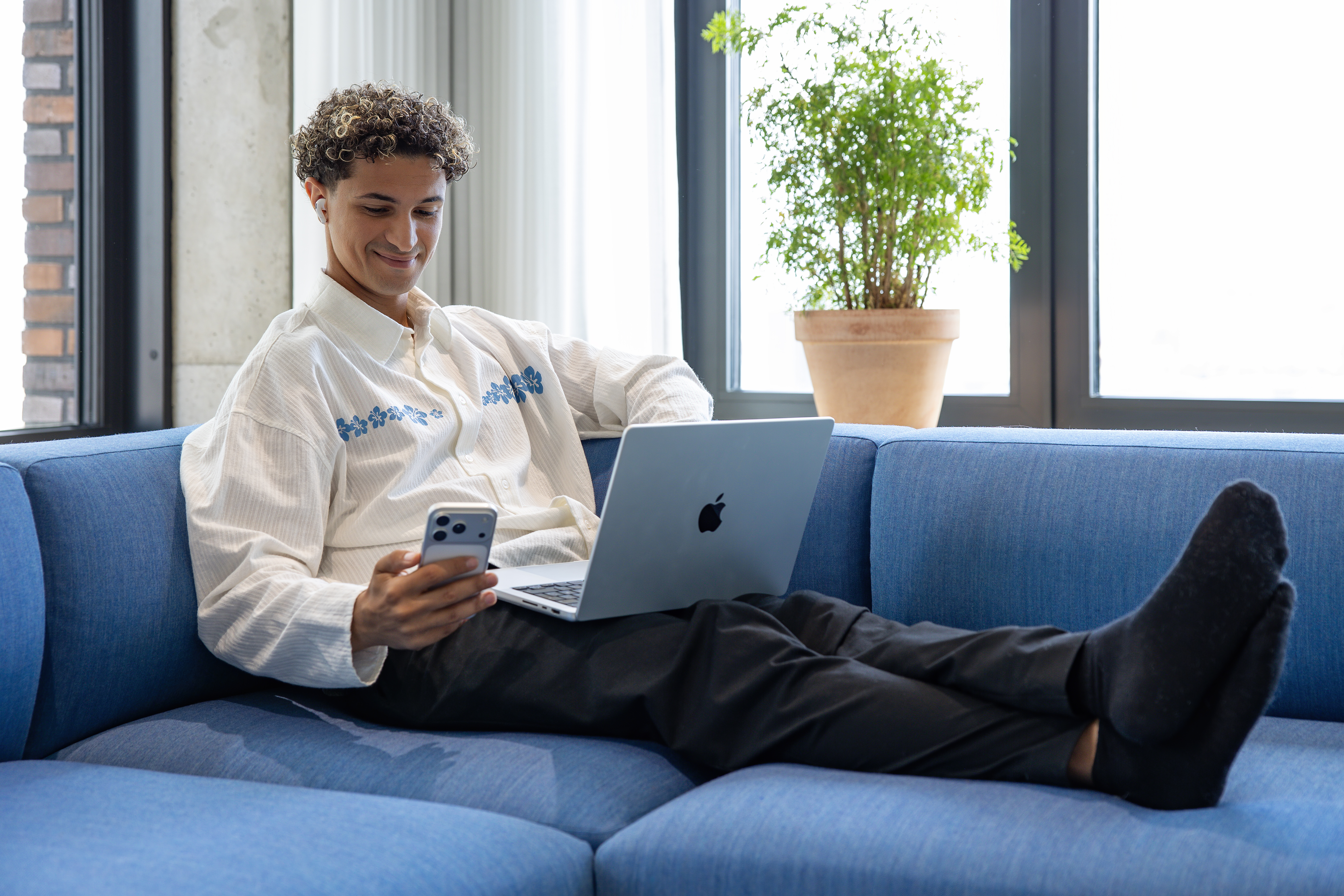 En mand sidder i en blå sofa med en computer og telefon
