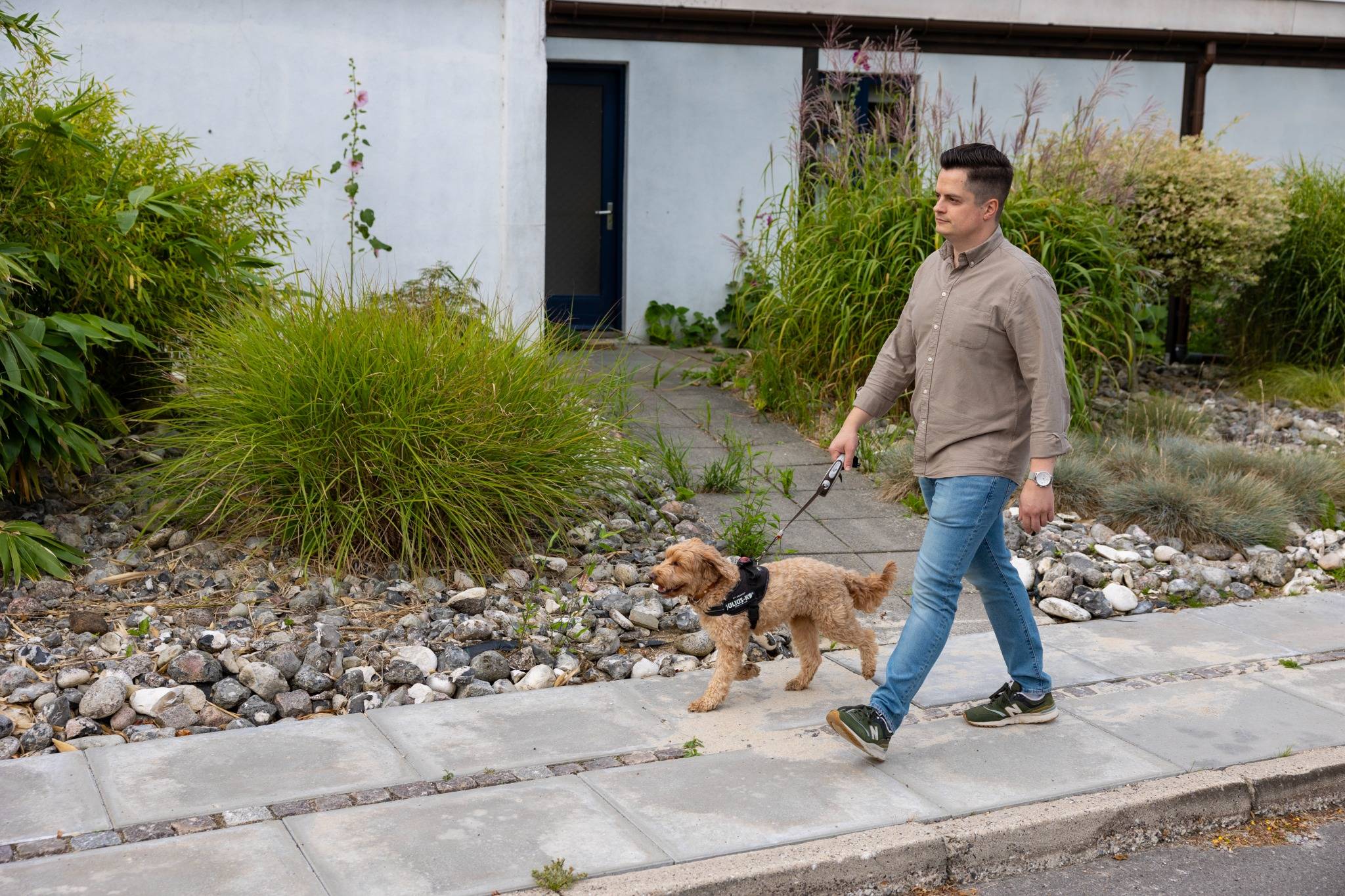 En mørkhåret mand, der går med sin lysebrune hund i snor udenfor. 