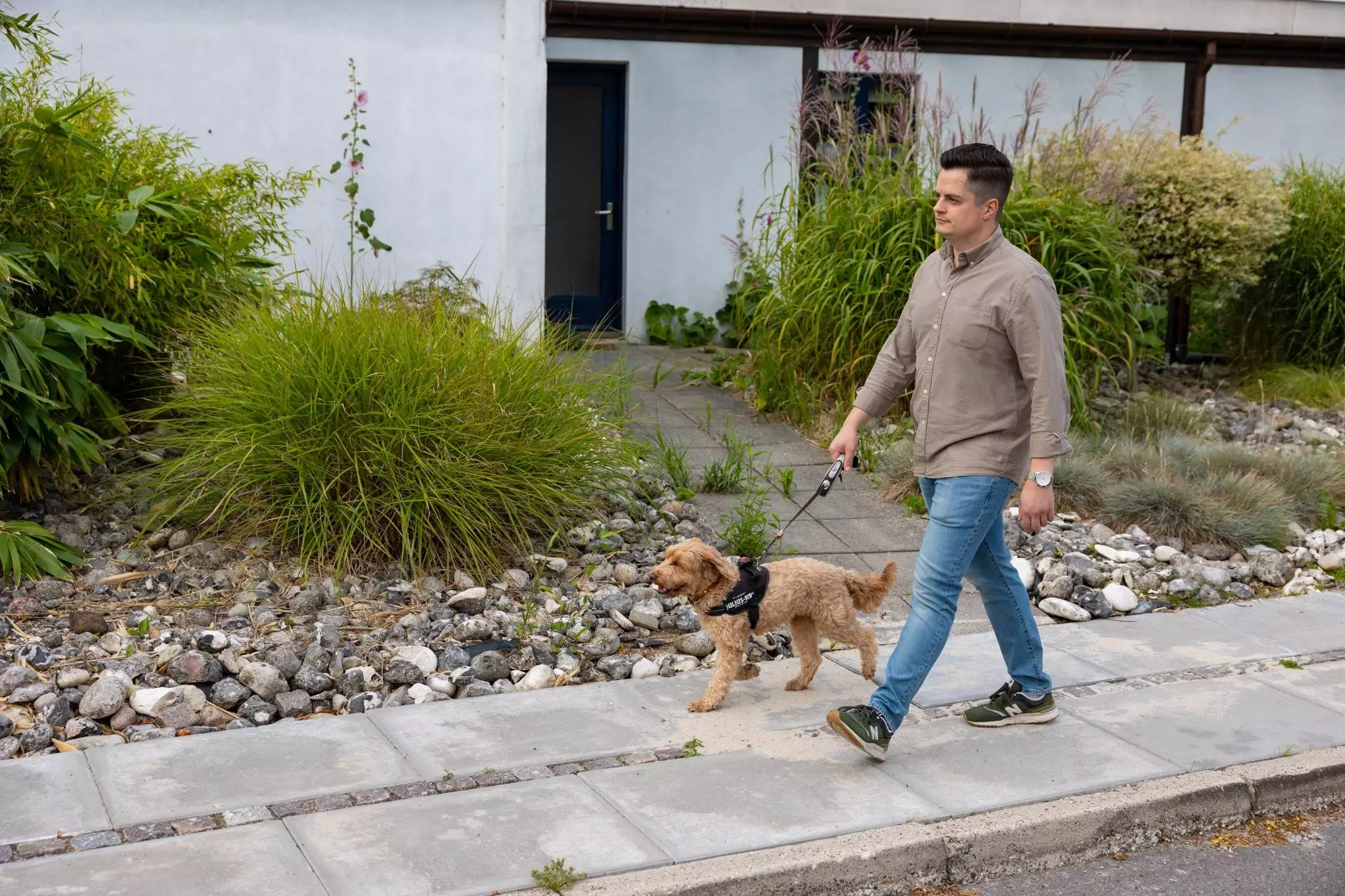 En mørkhåret mand, der går med sin lysebrune hund i snor udenfor.