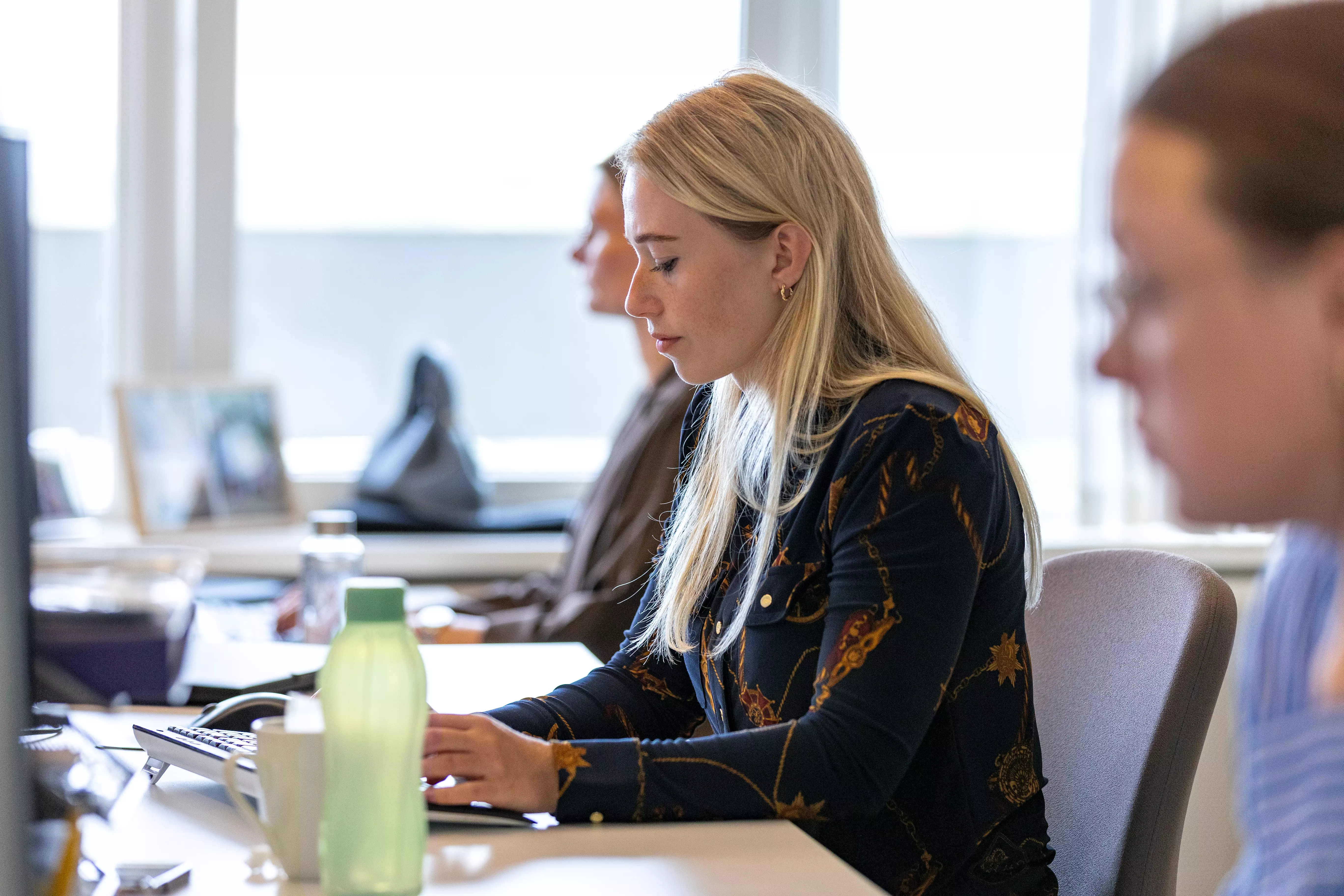 Tre kvinder sidder i et kontormiljø og arbejder