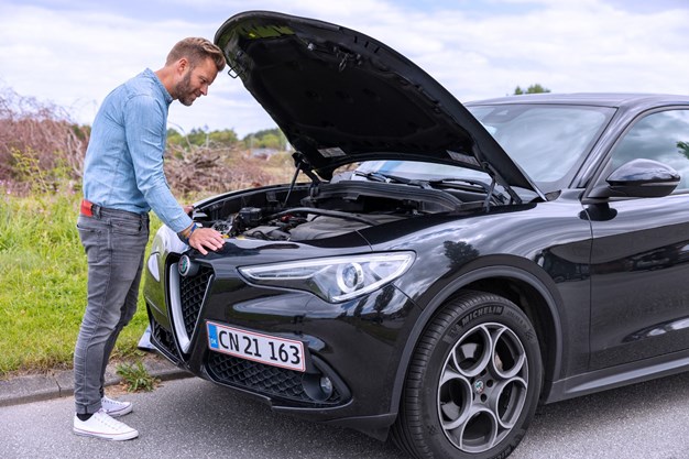 Mand kigger på motor i sort bil. Aros Forsikring vedligeholdelse.